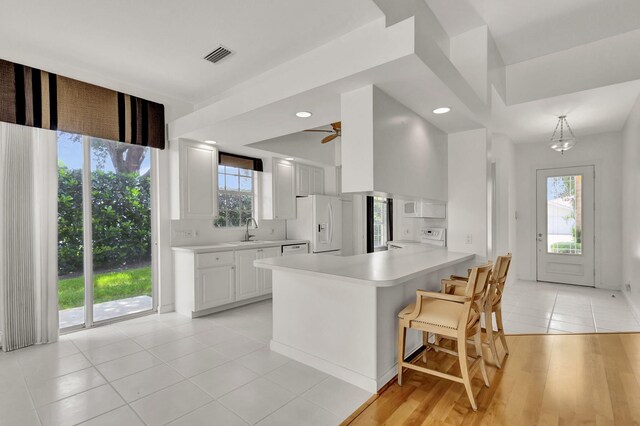 kitchen with a breakfast bar area, kitchen peninsula, light hardwood / wood-style flooring, and white appliances