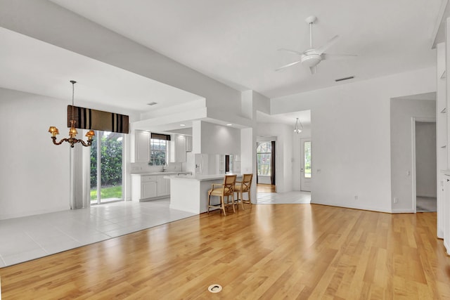 unfurnished living room with light wood-style floors, visible vents, and ceiling fan with notable chandelier