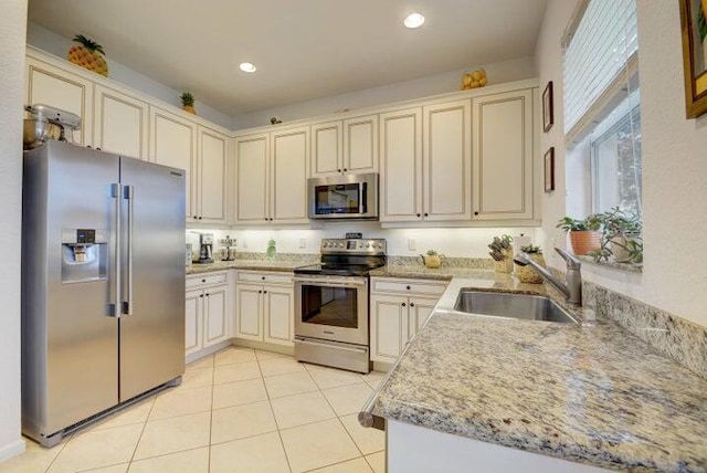 kitchen with light stone countertops, sink, cream cabinets, light tile patterned floors, and appliances with stainless steel finishes