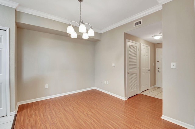 empty room featuring a notable chandelier, light wood-type flooring, and crown molding