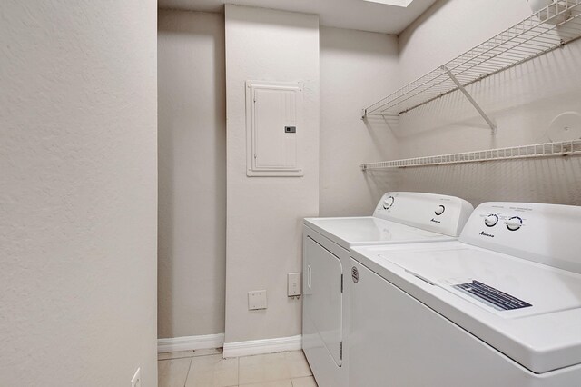 clothes washing area with electric panel, light tile patterned flooring, washing machine and dryer, and a skylight