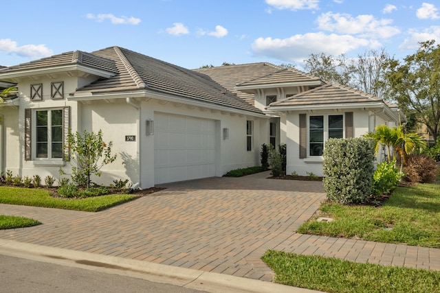 prairie-style house with a garage, a tile roof, decorative driveway, and stucco siding