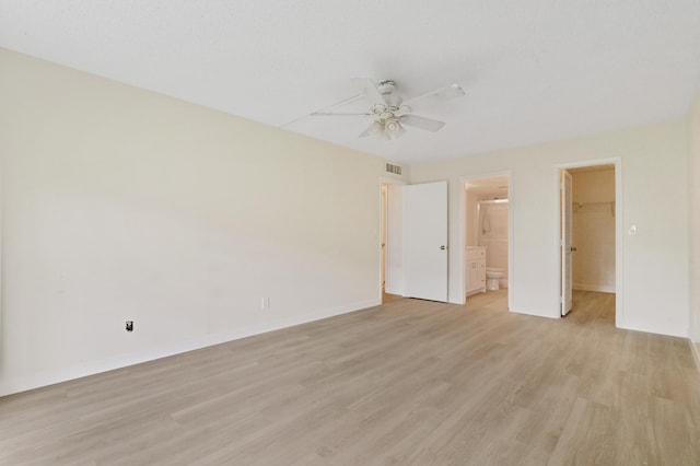 unfurnished bedroom featuring a spacious closet, a closet, ensuite bath, light hardwood / wood-style floors, and ceiling fan