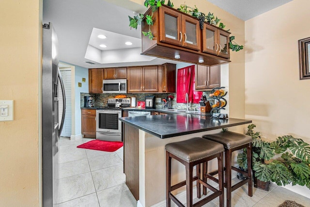 kitchen featuring tasteful backsplash, stainless steel appliances, kitchen peninsula, light tile patterned floors, and a kitchen breakfast bar