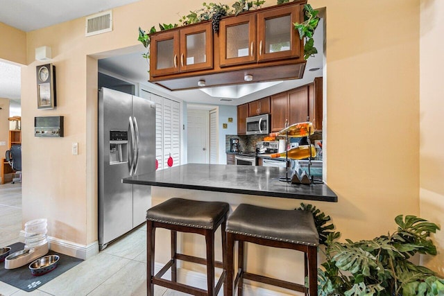 kitchen with light tile patterned flooring, appliances with stainless steel finishes, kitchen peninsula, and tasteful backsplash