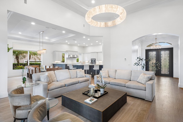 living room featuring light hardwood / wood-style flooring, french doors, crown molding, a tray ceiling, and sink