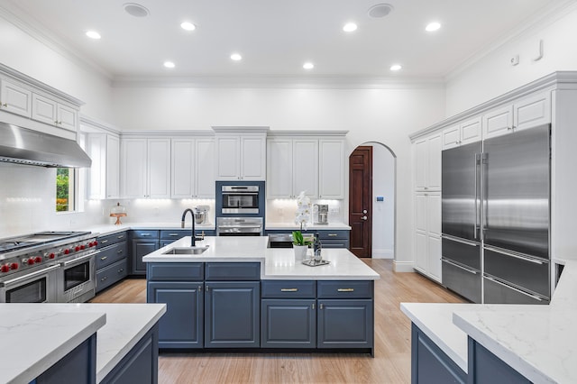 kitchen featuring a kitchen island with sink, tasteful backsplash, light wood-type flooring, and premium appliances