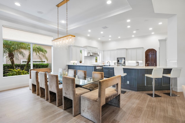 dining room featuring sink, a tray ceiling, crown molding, and light hardwood / wood-style floors