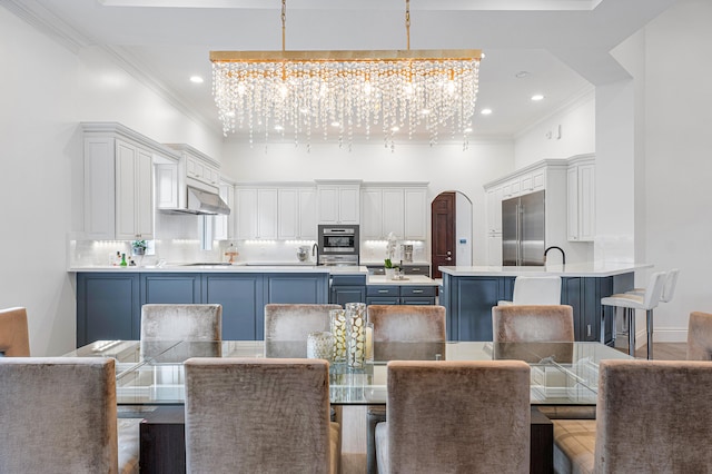 dining area with sink, wood-type flooring, ornamental molding, and an inviting chandelier