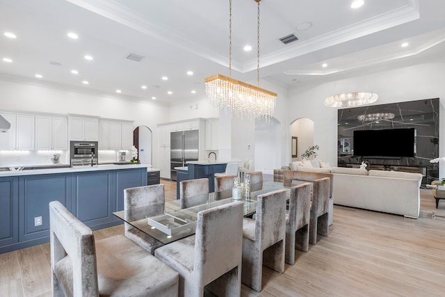 dining space featuring a tray ceiling, an inviting chandelier, light hardwood / wood-style floors, and crown molding