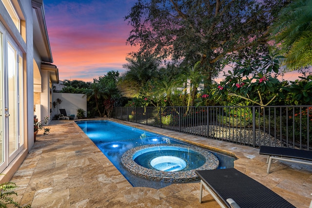 pool at dusk with an in ground hot tub and a patio area