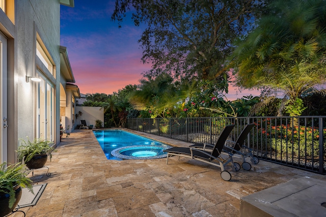 pool at dusk with an in ground hot tub and a patio area