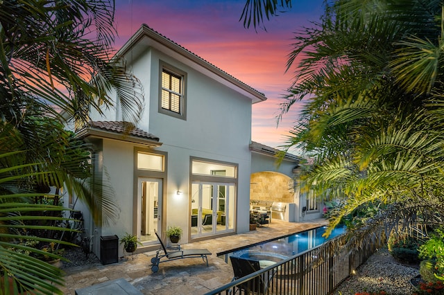 back house at dusk with a fenced in pool, french doors, and a patio area