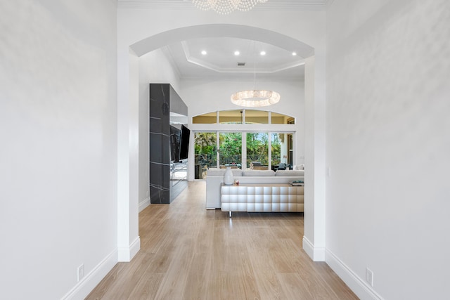 hallway with a raised ceiling, an inviting chandelier, ornamental molding, and light hardwood / wood-style floors