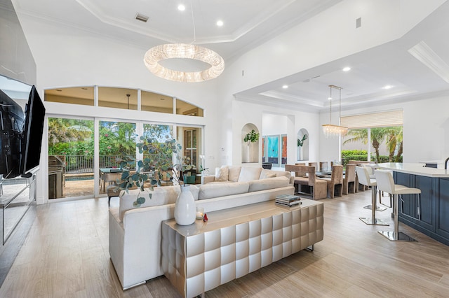 living room with a notable chandelier, light hardwood / wood-style flooring, a high ceiling, and a tray ceiling