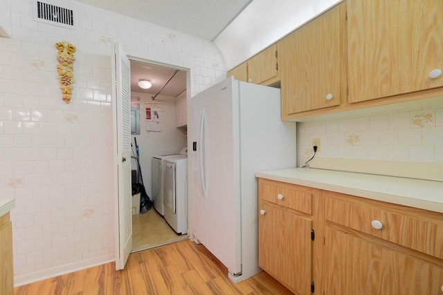 kitchen with washing machine and clothes dryer, light wood-type flooring, a textured ceiling, white refrigerator with ice dispenser, and tile walls