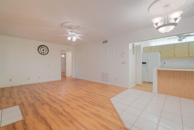 unfurnished living room with a textured ceiling, ceiling fan with notable chandelier, and light wood-type flooring