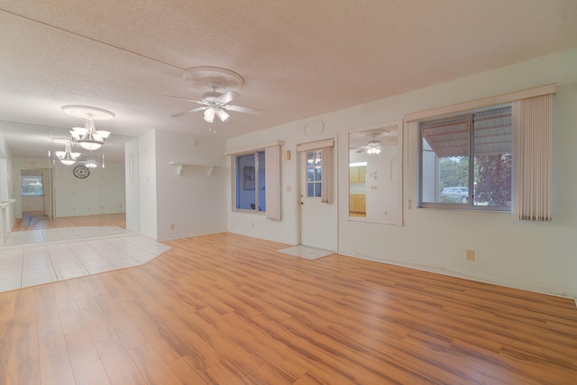 tiled spare room with ceiling fan with notable chandelier and a textured ceiling