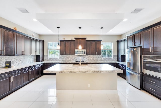 kitchen featuring dark brown cabinets, appliances with stainless steel finishes, a kitchen island with sink, and hanging light fixtures