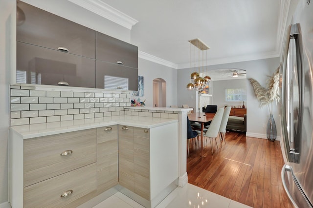 kitchen with hanging light fixtures, stainless steel refrigerator, ornamental molding, hardwood / wood-style flooring, and ceiling fan