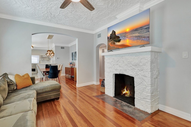 living room featuring a textured ceiling, ceiling fan with notable chandelier, wood-type flooring, ornamental molding, and a fireplace