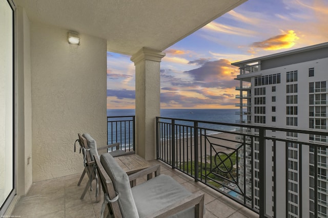 balcony at dusk featuring a water view