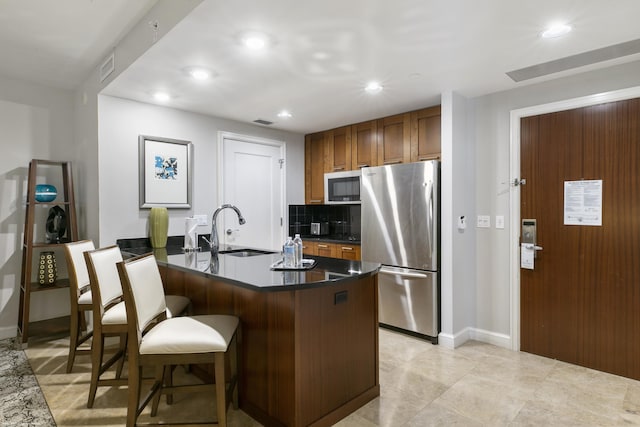 kitchen with a breakfast bar, sink, kitchen peninsula, stainless steel appliances, and decorative backsplash