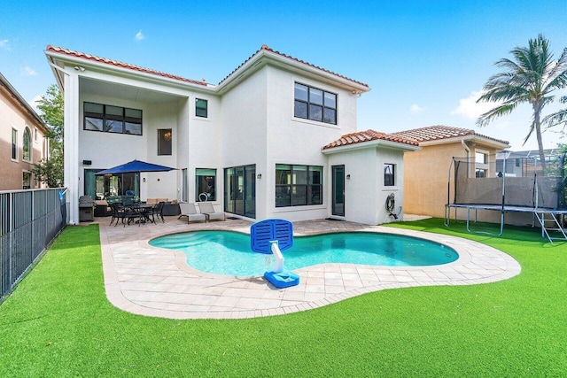 rear view of house with a trampoline, a patio, a fenced in pool, and a yard