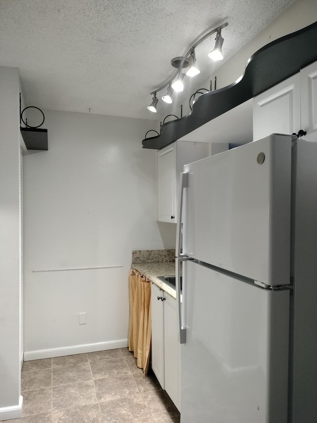 kitchen featuring a textured ceiling, white cabinets, white refrigerator, light tile patterned flooring, and rail lighting