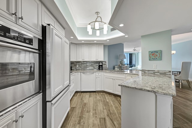 kitchen with white cabinetry, light stone counters, kitchen peninsula, a raised ceiling, and light hardwood / wood-style floors