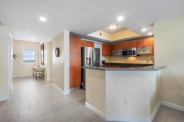 kitchen with appliances with stainless steel finishes, light wood-type flooring, kitchen peninsula, and a tray ceiling