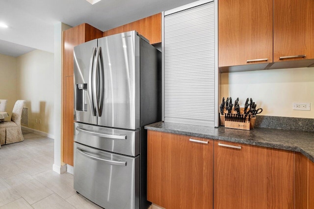 kitchen featuring dark stone counters and stainless steel fridge with ice dispenser