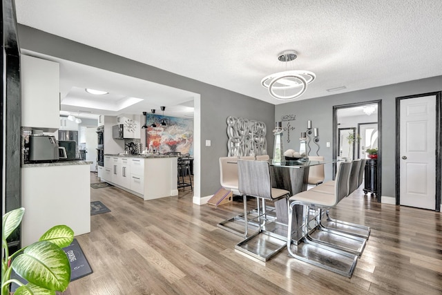 dining area with a textured ceiling, light wood-type flooring, and a tray ceiling