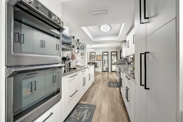 kitchen featuring light hardwood / wood-style floors, stone countertops, white cabinetry, white fridge, and a raised ceiling