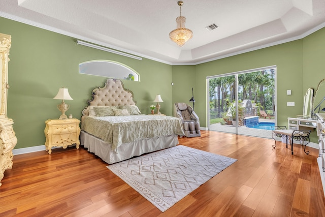 bedroom featuring a raised ceiling, access to outside, hardwood / wood-style floors, and ornamental molding