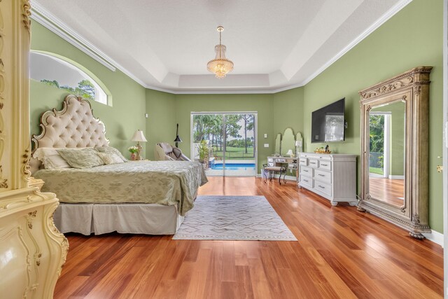 bedroom with hardwood / wood-style flooring, multiple windows, access to exterior, and a tray ceiling