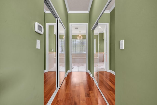 corridor with hardwood / wood-style flooring, a textured ceiling, a notable chandelier, and ornamental molding