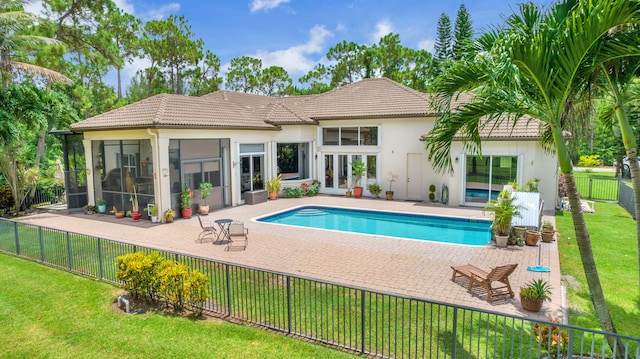 rear view of property featuring a fenced in pool, a yard, a patio area, a sunroom, and french doors