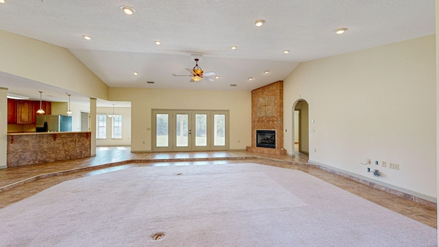 unfurnished living room featuring a fireplace, a textured ceiling, high vaulted ceiling, light carpet, and ceiling fan