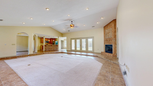 unfurnished living room with light tile patterned floors, ceiling fan, brick wall, a tile fireplace, and high vaulted ceiling