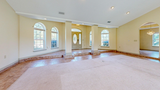 unfurnished living room with light tile patterned flooring, a chandelier, and ornate columns