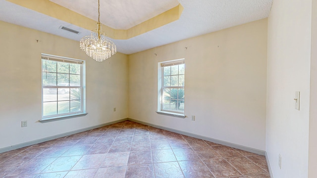 tiled spare room featuring a chandelier and a tray ceiling