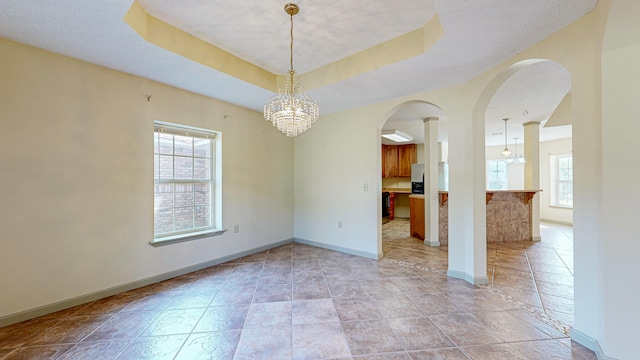 tiled spare room with a notable chandelier and a tray ceiling