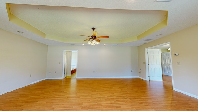 spare room featuring ceiling fan, light hardwood / wood-style flooring, and a tray ceiling