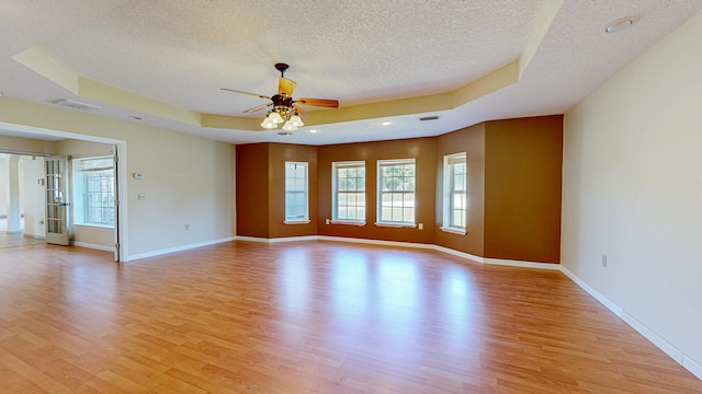 spare room with ceiling fan, a textured ceiling, light wood-type flooring, and a tray ceiling