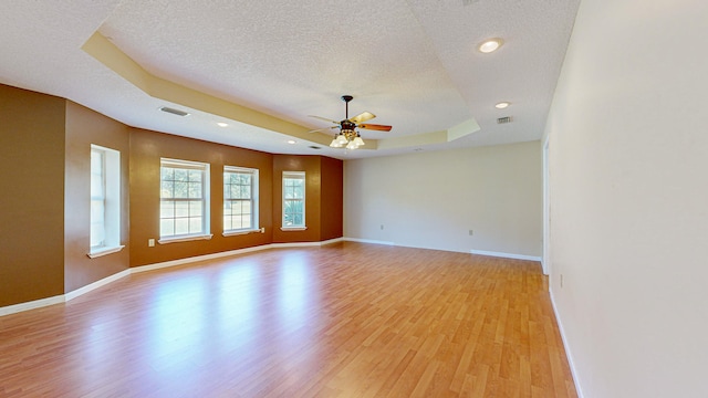 spare room with a textured ceiling, a raised ceiling, light wood-type flooring, and ceiling fan