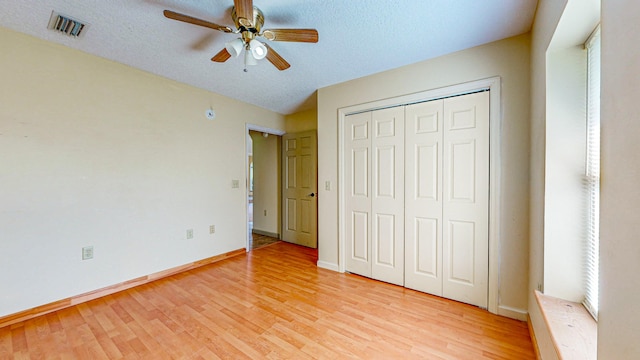 unfurnished bedroom featuring a textured ceiling, ceiling fan, light hardwood / wood-style floors, and a closet