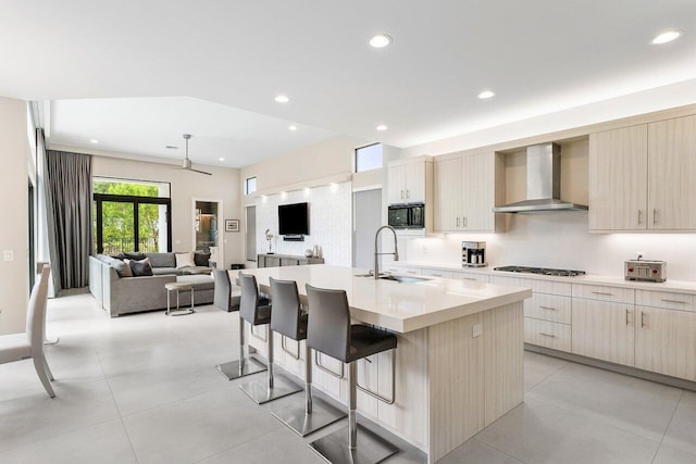 kitchen featuring sink, an island with sink, a kitchen bar, wall chimney exhaust hood, and black microwave