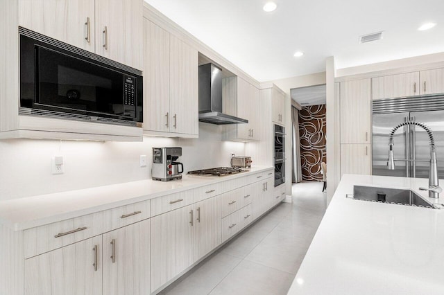 kitchen featuring light tile patterned flooring, sink, wall chimney exhaust hood, built in appliances, and light brown cabinets