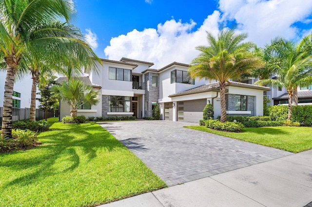 contemporary house with a front yard, fence, stucco siding, a garage, and decorative driveway